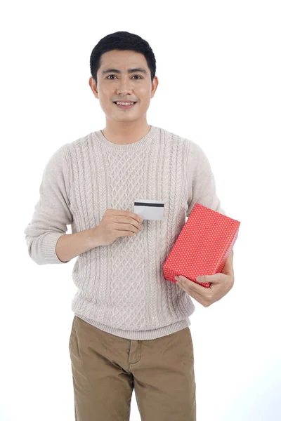 身穿灰色背景毛衣 手持红丝带礼品盒和信用卡或借记卡的亚洲年轻英俊男子 — 图库照片