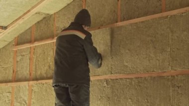 Çatının altındaki bir duvarda yalıtım yapan adam.