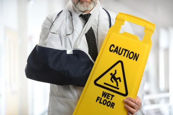 Doctor Wearing Elbow Sling Holding Caution Sign — Stock Photo, Image