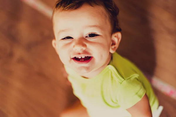 Porträtt av en leende bebis som tittar upp sittande på golvet med — Stockfoto