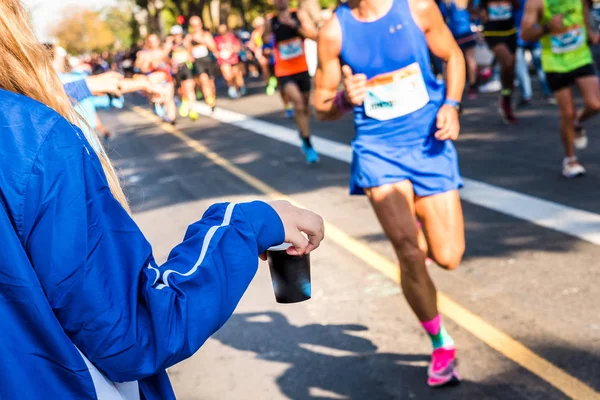 Volunteer offers an isotonic drink to a runner on a run. — Stock Photo, Image
