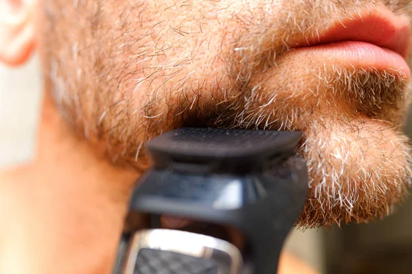 A man shaves his beard using an electric razor. — Stock Photo, Image