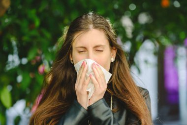 Kahverengi saçlı kadın burnunu silmek ve temizlemek için mendil kullanıyor.