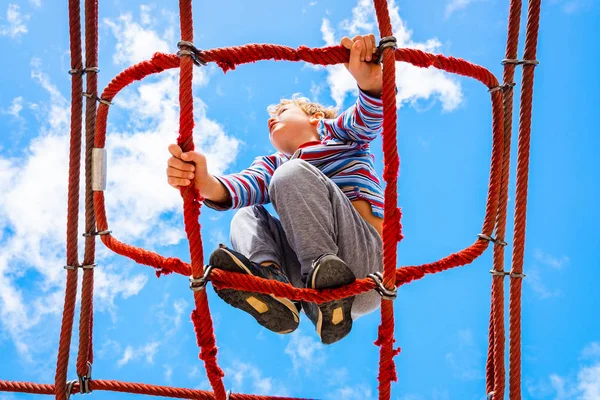 Blonďatý chlapec sedící na pavučinovém žebříku v dětském — Stock fotografie