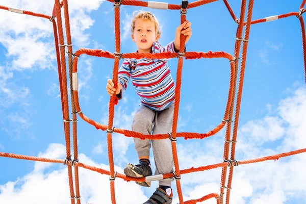 Blonder Junge, der auf einer Seilleiterkonstruktion im Kinderzimmer hockt — Stockfoto
