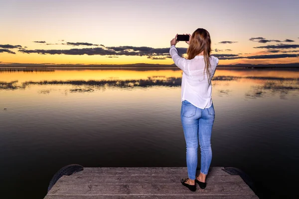 Young woman taking a selfie picture with her cell phone in a bea