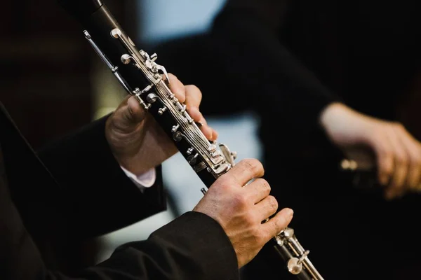 Clarinete segurando uma flauta transversal de metal em suas mãos. — Fotografia de Stock