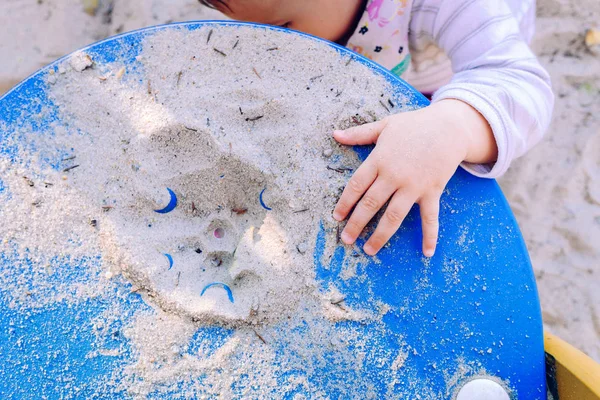 Um bebê brinca com areia em uma areia, colocando a mão para agarrar . — Fotografia de Stock
