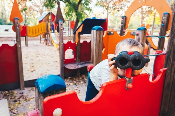 Niño jugando en un patio de recreo, mirando a través de binoculares falsos . —  Fotos de Stock