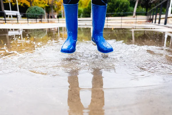 Boy with blue water boots jumps in a puddle.