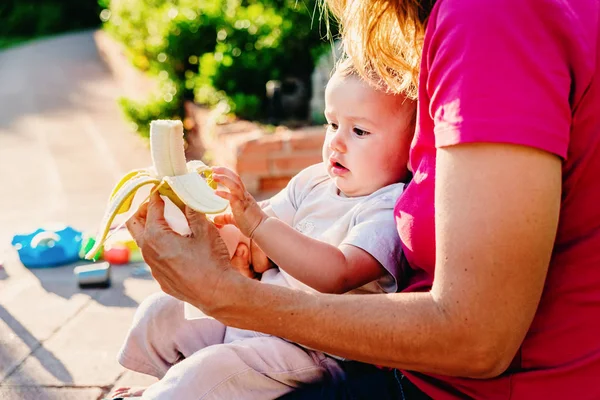 Adorable bebé con cara divertida al tratar de morder un plátano a f — Foto de Stock