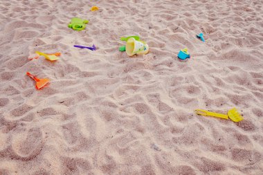 Kürekler ve plastik oyuncaklar bir kum havuzunda terk edilmiş, kirlenmiş.