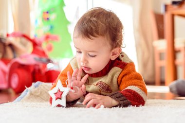 Bebek Noel parçaları ile evin halısında yatıyor..