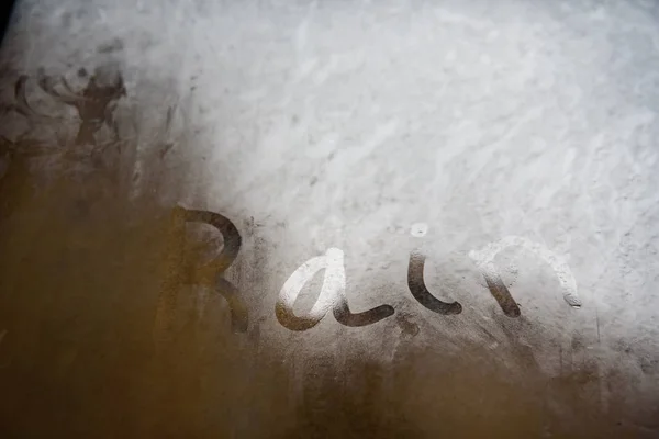 Lluvia de palabra escrita sobre cristales húmedos con niebla en un día lluvioso de invierno — Foto de Stock