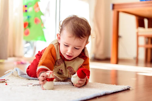 Baby plays lying on the house carpet with Christmas pieces.