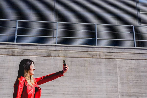 Chica en chaqueta de cuero rojo tomando una foto selfie, con su propia s — Foto de Stock