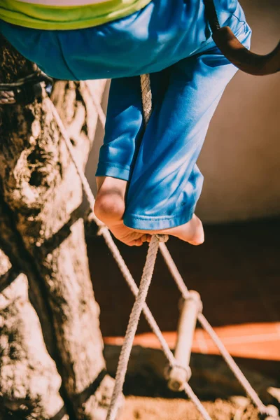 Los pies desnudos de un niño aferrado a una cuerda mientras trepa por ella . —  Fotos de Stock