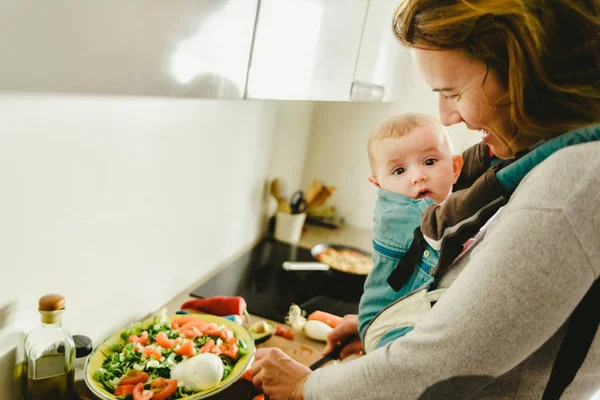 Busy mother preparing food in the kitchen while taking care of h — Stock Photo, Image