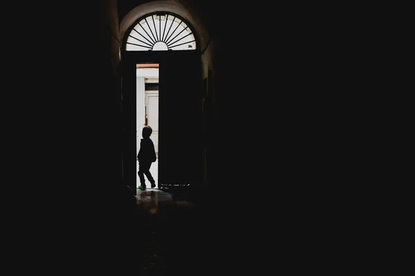 Kind geht durch eine hinterleuchtete Tür, Konzept der Einsamkeit ein — Stockfoto