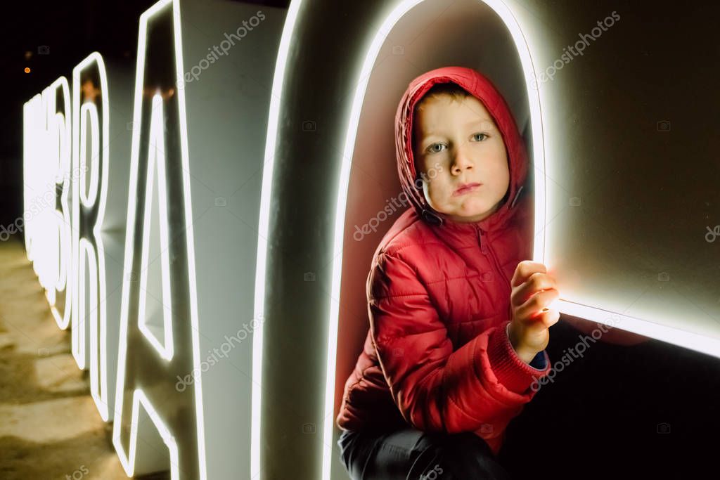 Child peeking at night to large white neons.