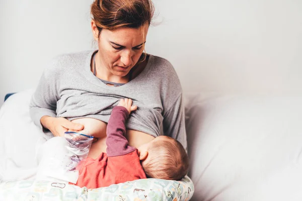 Mother breastfeeding her newborn baby while pumping milk from he — Stock Photo, Image