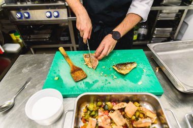 Aşçı olan bir restoranın mutfağı tepsilere balık koyuyor.