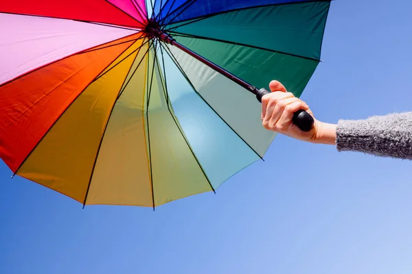 Mulher segura um guarda-sol multicolorido em um dia de verão com céu azul — Fotografia de Stock