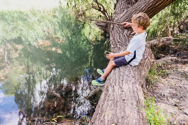 Nehrin kıyısındaki kütükte balık tutan bir çocuk.. — Stok fotoğraf