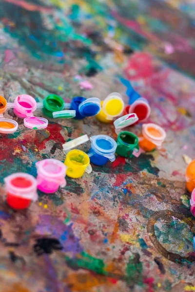 Fondo, latas de pintura en la mesa manchada de muchos colores . — Foto de Stock