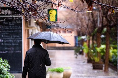 An adult man walked down the street of a city with a black umbre