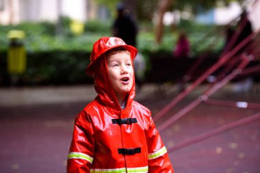 Boy dressed as a fireman with red raincoat splashes on the grass