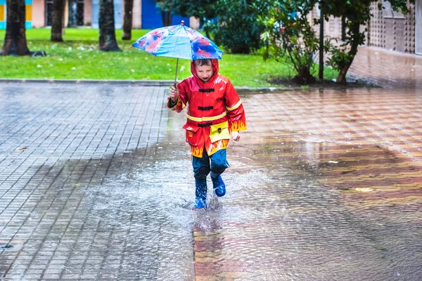 Boy with red raincoat disguised with umbrella splashes in a pudd — 图库照片