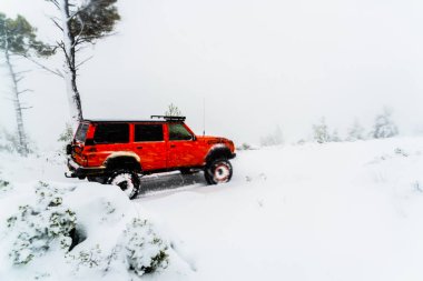 Red 4x4 off-road car on a snowy road during heavy snowfall.
