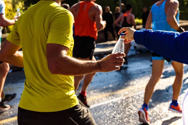 Una mano consegna una bottiglia d'acqua ad un corridore in un runni — Foto Stock