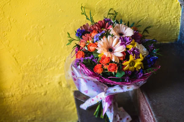 Fin bukett med blommor lutande på en grov gul vägg. — Stockfoto