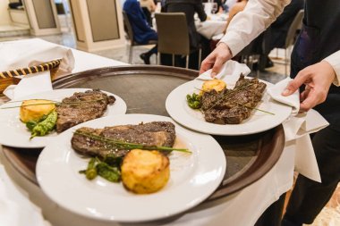 Waiter picks up a plate with a meat steak during a dinner at a r
