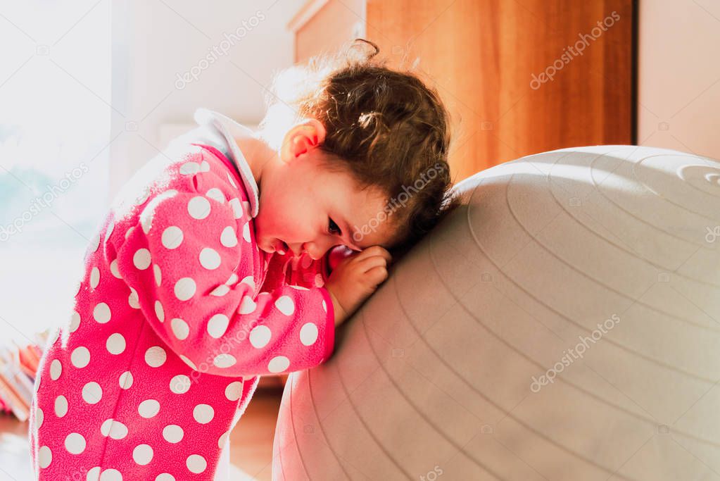 Shy baby is hidden from looks, dressed in pink pajamas in her bedroom.