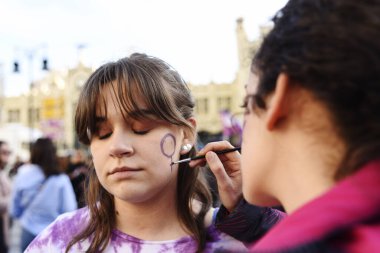 Valencia, Spain - October 8, 2020: Young woman paints her face with the feminist sign during protests claiming equal rights.