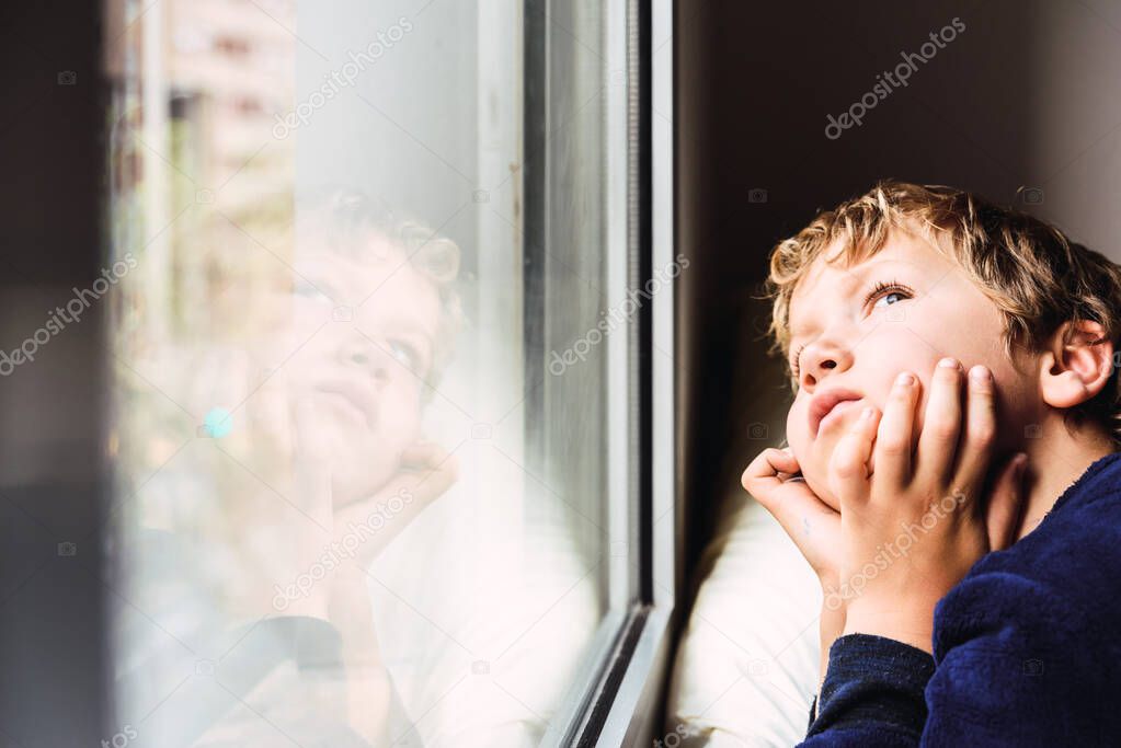 Boy confined at home by the coronavirus crisis in Spain, looks bored out the window without being able to leave home.