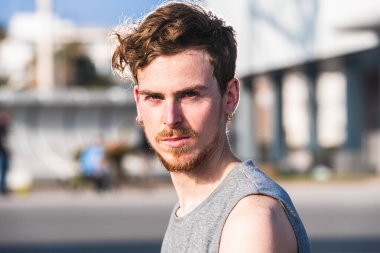 Genç, konsantre olmuş kızıl saçlı adam gün boyunca kazakla egzersiz yapıyor kulaklarında küpeler, yakın plan portresi, odaklanmamış arka plan..