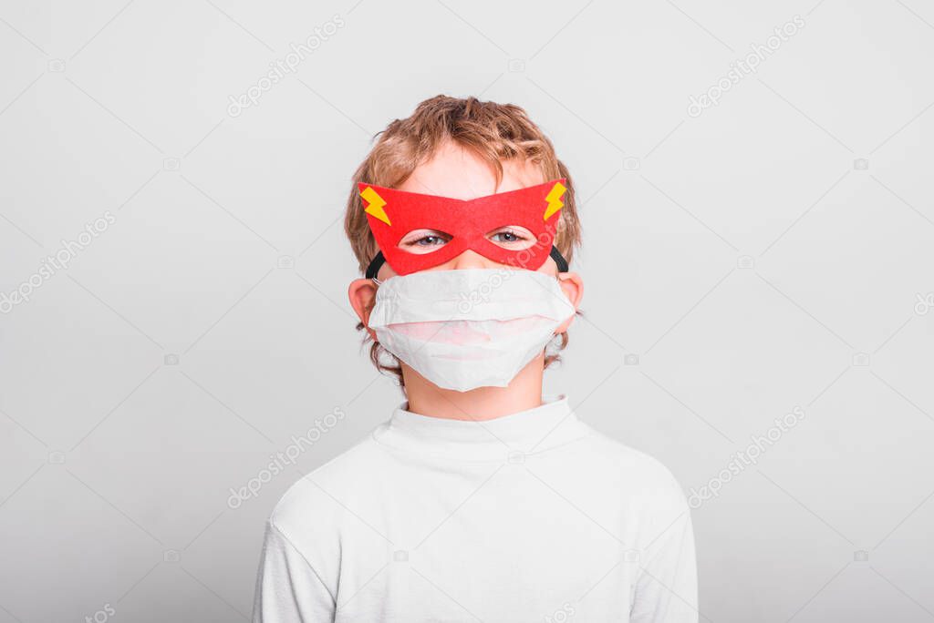 Portrait of boy in superhero mask with his mouth covered with a medical mask to protect himself from viral infections and diseases.