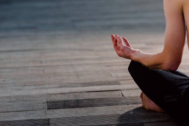 Genç bir yogi, nilüfer çiçeğinde tahta üzerinde otururken ellerini dizlerinin üzerine koyar. Boşluğu kopyala