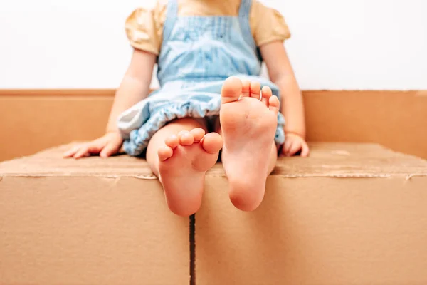 Bare feet of a girl sitting on a pile of cardboard.