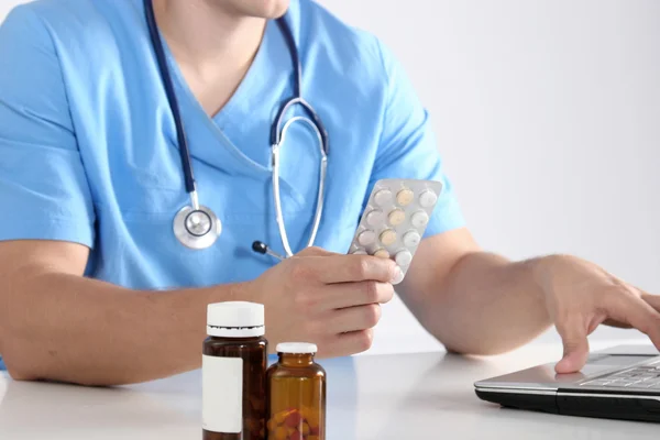 Médico sentado à mesa e segurando o frasco — Fotografia de Stock