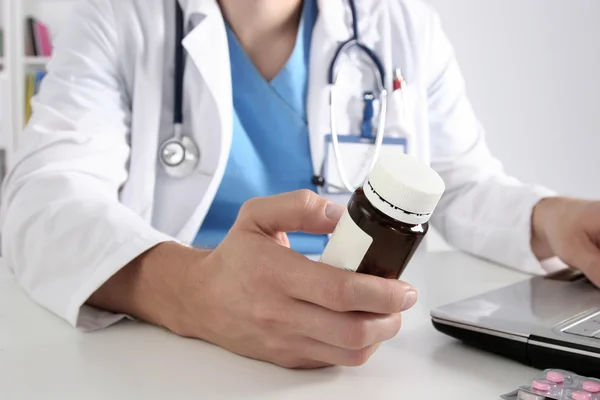 Médico sentado à mesa e segurando o frasco — Fotografia de Stock