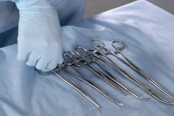 Closeup doctor hands of four different stainless steel surgical forceps and scalpel isolated on white background