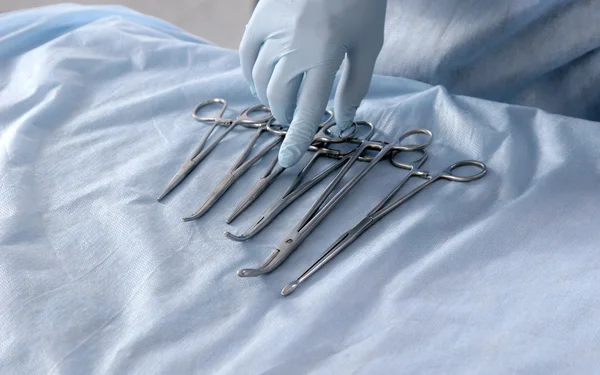 Mãos de médico close-up de quatro pinças cirúrgicas de aço inoxidável diferentes e bisturi isolado em fundo branco — Fotografia de Stock