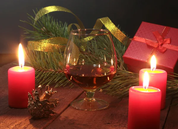 Composición navideña con coñac de vidrio, caja de regalo y vela sobre mesa de madera —  Fotos de Stock