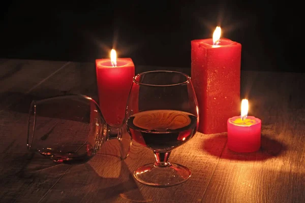 Glass of cognac and red candle on a wooden background — Stock Photo, Image