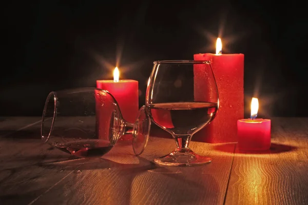 Стакан коньяка и красной свечи на деревянном фоне — стоковое фото